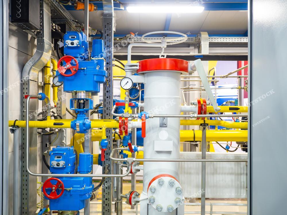 Фотография комплекса газораспределительной системы с фильтрационным оборудованием в центре, окруженным желтыми трубами и синими управляющими узлами с красными рукоятками. Установка предназначена для обеспечения фильтрации и контроля подачи газа на производственных объектах.